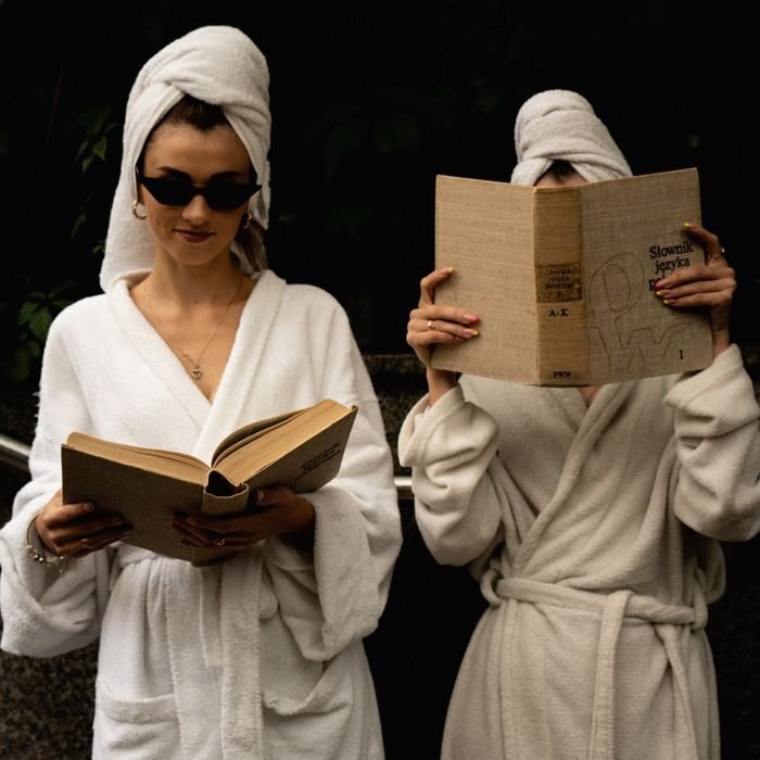 Two women in bathrobes enjoy reading books outdoors, capturing a relaxed lifestyle moment.